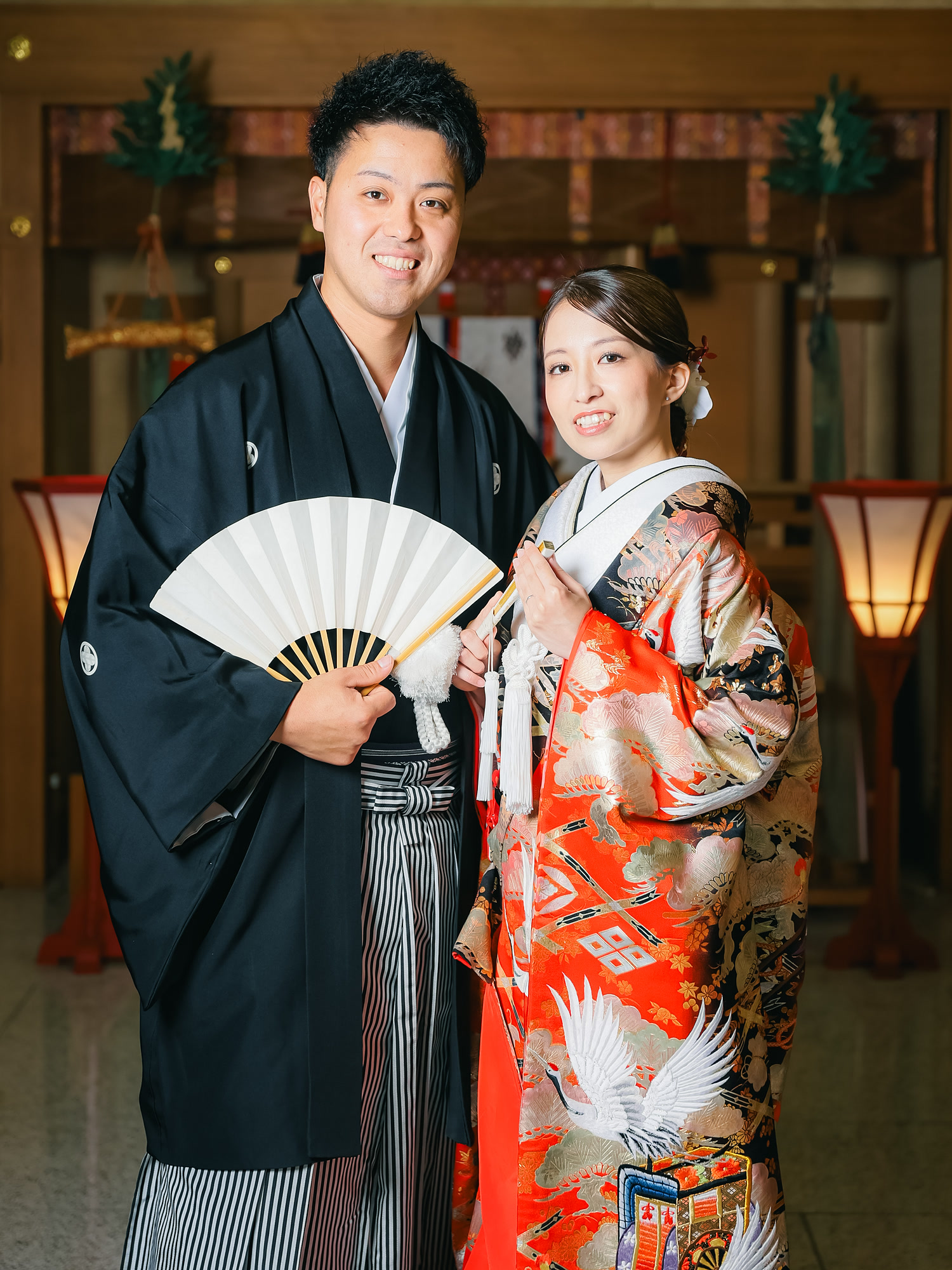 Bride in a crane-patterned iro-uchikake kimono holding a folding fan inside a shrine hall